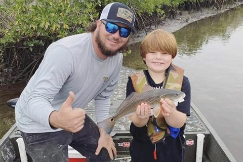 Young Child Holding Fish with Captain While Mudboat Fishing